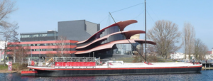 Das Theaterschiff Potsdam vor dem Hans Otto Theater (Foto: wikipedia.de Biberbaer, Lizenz: CC BY-SA 3.0 https://creativecommons.org/licenses/by-sa/3.0)